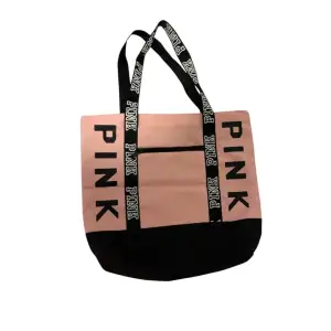 Snygg shoppingväska i rosa och svart från Pink. Väskan har svarta handtag med texten 'PINK' i vitt och en praktisk dragkedja framtill. Perfekt för att bära med sig allt man behöver under dagen. Får plats med mycket😻🙏🏻
