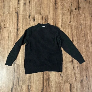 Mörkgrå stickad tröja från Zara - Säljer en stilren mörkgrå stickad tröja från Zara med långärmad design. Perfekt för kyligare dagar och enkel att matcha med olika outfits. Tröjan har en klassisk passform och ribbade muddar vid ärmslut och nederkant.