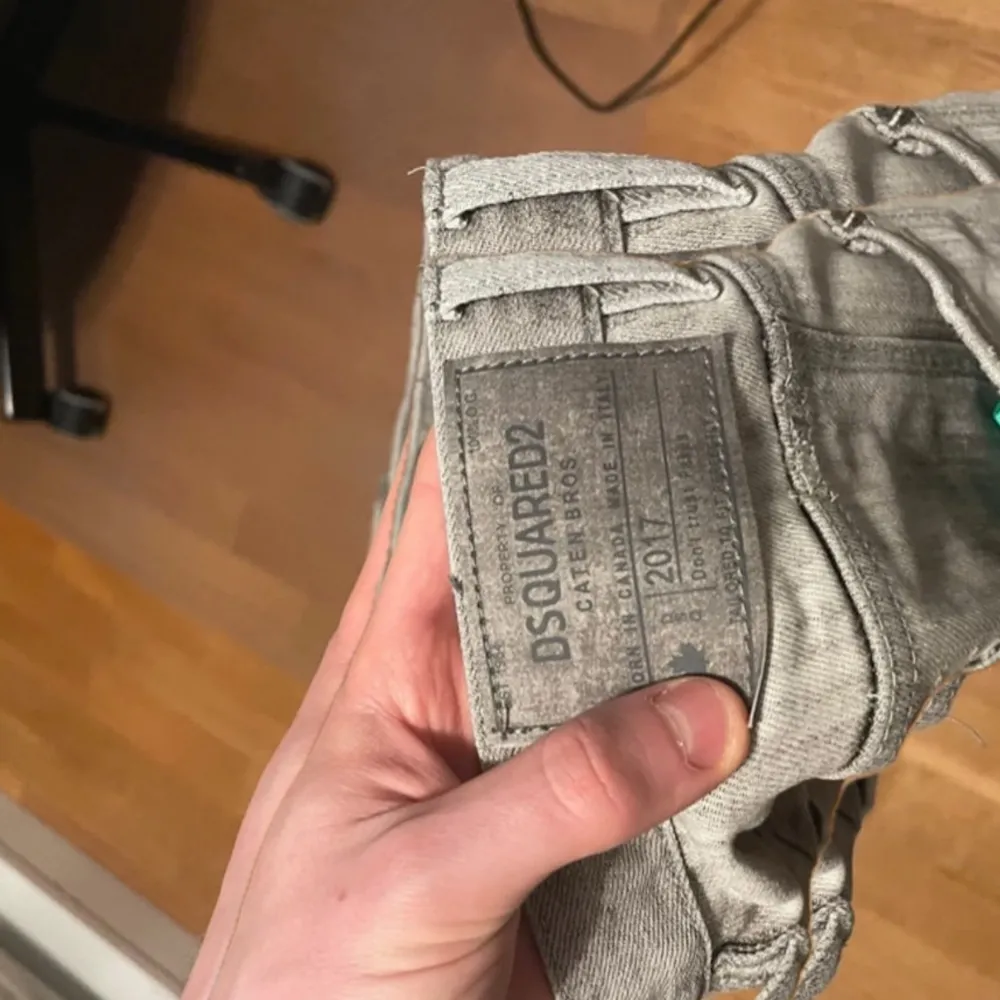 Säljer ett par grå jeans från Dsquared2 med slitna detaljer och en cool, tvättad look. Byxorna har en knappgylf och en röd etikett med märkesnamnet vid gylfen. Perfekta för en avslappnad stil.. Farkut & Housut.