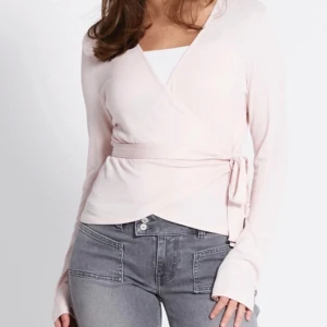Ljusrosa topp - Säljer en stilren ljusrosa omlottopp med knytband i midjan. Toppen har långa ärmar och en v-ringad design som ger en elegant look. Perfekt för en chic vardagsstil.