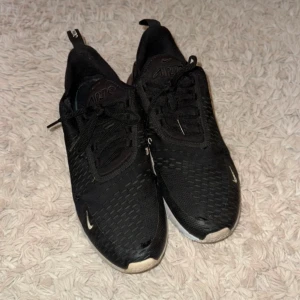 Svarta Nike sneakers - Säljer ett par svarta Nike sneakers med snörning och rund tå. Skorna har en sportig design med en vit sula och små vita detaljer. Perfekta för träning eller vardagsbruk.