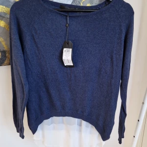 Blå tröja med vit detalj från ONLY - Säljer en snygg blå tröja från ONLY med en unik vit detalj i nederkant. Tröjan har långa ärmar och en rund halsringning. Perfekt för en stilren look. Passar bra till både jeans och kjol.