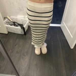 Randig långkjol med slits - Snygg långkjol i vitt med svarta ränder. Kjolen har en slits på sidan och är ribbad för en bekväm passform. Perfekt för en stilren look.