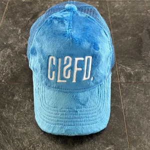 Blå pälsig keps från Classified - Snygg blå keps med pälsig framsida och mesh på baksidan från Classified. Broderad text framtill ger en cool touch. Perfekt för att sticka ut i mängden jag har inte använt den överdrivet mycket och försökt ta hand om den, därför skulle jag säga att skicket är 8/10! Det ända ät att det finns en liten nästa osynlig fläck på toppen av kepsen .Den är köpt för 599 och finns inte att köpa nu längre! Påse ingår.