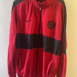 Röd träningsjacka från Nike - Säljer en snygg röd träningsjacka från Nike med PSG-logga på bröstet. Jackan har en dragkedja framtill och svarta detaljer. Perfekt och har inget fel på sig. Priset går diskuteras