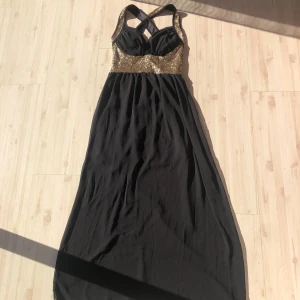 Balklänning svart  - Svart lång balklänning med guldpaljetter på överdelen och korsade axelband