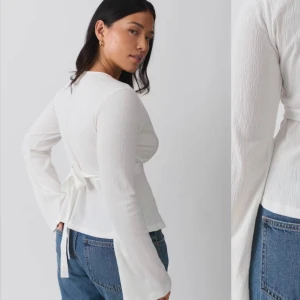 Vit omlottopp med knytband - Säljer en stilren vit omlottopp med långa ärmar och knytband i midjan. Toppen har en v-ringad design och är perfekt för en chic look. Passar bra till både jeans och kjol.
