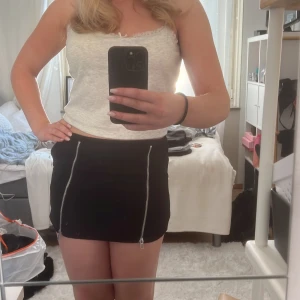 Svart kortkjol med dragkedjor - Snygg svart kortkjol med två framträdande dragkedjor framtill. Perfekt för en trendig look.