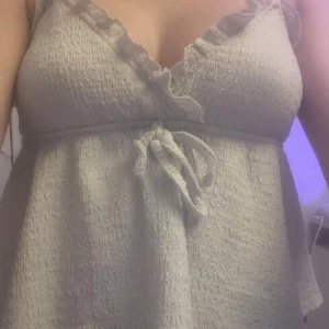 Vitt linne med volanger  - Vitt linne med volangdetaljer vid halsringningen och knytband i midjan. Helt okej skick och inga skador bara använts mycket men annars fint