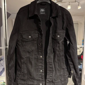 Svart jeansjacka från ZARA - Snygg svart jeansjacka från ZARA med knappar framtill och två bröstfickor med lock. Perfekt för en stilren look.