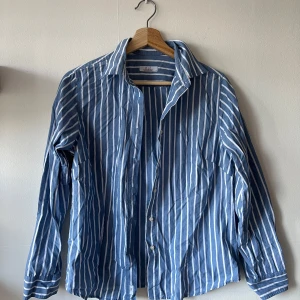 Blå och vit randig skjorta från OLÉ - Säljer en snygg blå och vit randig skjorta från OLÉ. Skjortan har långa ärmar och knappar framtill. 