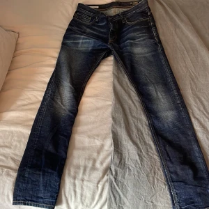 Blå slim fit jeans från Jack & Jones - Snygga blå jeans från Jack & Jones Originals, modell Tim Slim Fit. Jeansen har klassisk femficksdesign, kontrastsömmar och en cool tvätt med slitningar. Passformen är slim och materialet är robust denim i bomull. Perfekt för dig som gillar en modern och stilren look. Priset kan diskuteras då de finns ett litet hål som går lätt att fixa vid grenen🤗