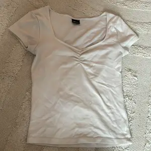 Säljer en stilren vit topp från Sinatricot med u-ringning och rynkdetalj framtill. Toppen har korta ärmar och är perfekt för en enkel och snygg look. Passar bra till både jeans och kjol. 🌟