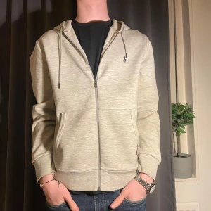 Ralph lauren hoodie - Säljer en stilren grå hoodie med dragkedja och huva. Den har långa ärmar och praktiska fickor framtill. Perfekt för en avslappnad look. I storlek M