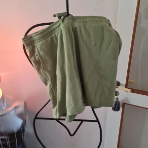 Gröna shorts från H&M - Säljer ett par gröna shorts från H&M i regular fit. De är tillverkade av en bomulls- och polyesterblandning och har en bekväm elastisk midja med knytband. Perfekta för en avslappnad stil.