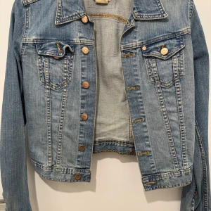 Jeansjacka från &Now - Snygg jeansjacka från &Now i en klassisk blå tvätt. Jackan har knappar framtill och två bröstfickor med lock. Perfekt för en avslappnad stil.