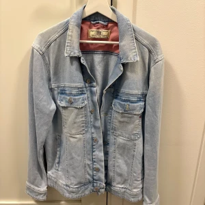 Ljusblå jeansjacka från Replay - Snygg ljusblå jeansjacka från Replay med klassisk design och knappar framtill. Jackan har två bröstfickor med lock och knapp, samt en läderpatch med Replay-logga på baksidan. Perfekt för en avslappnad stil. Priset kan diskuteras.