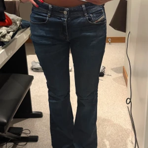 Diesel bootcut jeans i mörkblå denim - Snygga mörkblå jeans från Diesel med klassisk femficksdesign och bootcut-ben. Jeansen har låg midja, diskreta slitningar och logotypdetalj på fickan. Tillverkade i stretchig denim för skön passform. Perfekta för dig som gillar retrovibe och markerade ben.