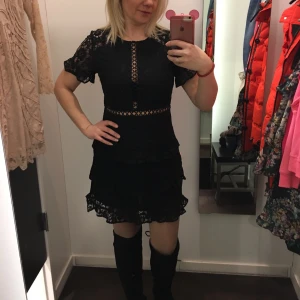 Svart spetsklänning med volanger - Supersnygg svart kortklänning i spets med volangdetaljer och genombrutna partier vid midja och bröst. Klänningen har korta ärmar och en feminin v-ringad design framtill. Perfekt för dig som gillar detaljer och en cool look. Hrlt ny,bars tvättad