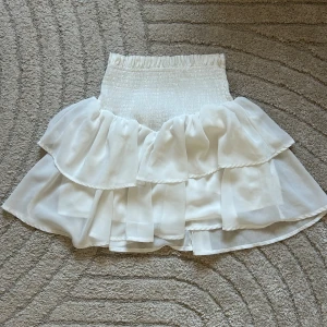 Vit volangkjol - Superfin vit kjol från SHEIN med volanger och smock i midjan. Fluffig, lätt och perfekt till sommaren, fest eller bara en fin vardagslook. Kjolen är i toppskick, använd väldigt lite känns och ser ut som ny. Dock kan du köpa båda för ett bättre pris!☺️