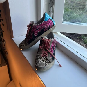 BiBi LOU leopardiga glitter skor  - Unika sneakers från BiBi LOU med rosa glitterpaneler, leopardmönstrad tå och blå lackdetaljer på hälen. Skorna har oranga snören, kommer med grå också, och en platt sula. Perfekt för dig som vill sticka ut med färg och mönster. Tyvärr fått litet hål på baksidan av hälen men läcker inte in, Storlek 37 men jag som har storlek 48 passar de jätte bra ❤️