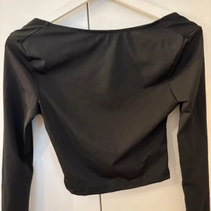 Svart öppenrygg tröja - Säljer en svart öppen rygg tröja. Toppen har en croppad passform och är tillverkad i ett mjukt material som sitter snyggt på kroppen. Perfekt för dig som gillar stilrena och trendiga plagg.