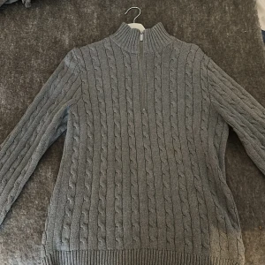 Grå stickad tröja Selected Homme - Säljer en grå kabelstickad tröja från Selected Homme med half zip och hög krage. Tröjan har långärmade ribbade muddar och är gjord i mjukt stickat material. Perfekt för dig som gillar klassisk stil med modern touch.