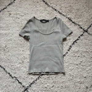 Ljusgrå ribbad topp från lager 157 - Supersnygg ljusgrå ribbad topp från lager 157 med korta ärmar och rundad, djup urringning. Tight passform som sitter snyggt och passar perfekt till jeans eller kjol. Enkel och stilren design som är lätt att matcha.