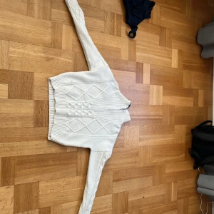 Vit stickad kofta med mönster från C - Säljer en vit stickad kofta från Cubus i storlek S. Tröjan har ett snyggt kabelstickat mönster med diamantformer på framsidan och ribbade muddar. Långärmad och perfekt för kyliga dagar. Passar dig som gillar klassisk och clean stil.