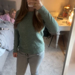 Grön stickad tröja från Vero Moda - Mysig grön stickad tröja från Vero Moda i storlek XS. Tröjan har rund hals, ribbade muddar och lång ärm. Perfekt att slänga på sig när det är lite kyligt ute. Enkel och stilren design som funkar till jeans eller kjol.