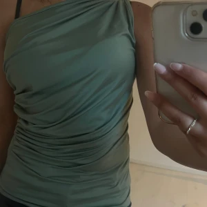 Grön oneshoulder topp  - Snygg ljusgrön oneshoulder topp med draperad effekt och tight passform. Säljer då den är för stor för mig. Strl s.