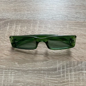 Gröna rektangulära solglasögon - Snygga gröna solglasögon med rektangulär form och transparent båge. Glasen är tonade i grönt och bågarna likaså. Perfekt accessoar för dig som vill ha en unik look och gillar trendiga detaljer. Vet ej märket. Använt fåtal gånger.