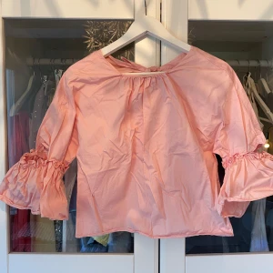 Rosa blus med volangärmar - Supersöt ljusrosa blus med breda volangärmar och snygg knytning i nacken. 