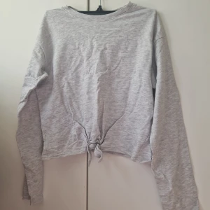 Grå långärmad tröja med knyt från H&M - Säljer en ljusgrå långärmad tröja från H&M i storlek 152. Den är väldigt bekväm. Jag tyckte om den väldigt mycket som barn. 