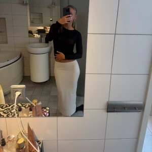 Vit långkjol med tight passform - Säljer en stilren vit långkjol med tight passform. Kjolen är enkel och rak i modellen, utan synliga detaljer eller mönster. Materialet känns mjukt och följsamt, perfekt för dig som gillar minimalistisk och clean stil. Har ett litet hål men syns knappt 