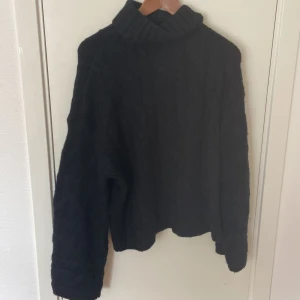 Svart polotröja från Bik Bok - Mysig svart polotröja från Bik Bok i stickat material. Tröjan har en hög krage och ett klassiskt kabelstickat mönster. Passformen är loose och den har långa ärmar, perfekt för kyliga dagar. Enkel att matcha med jeans eller kjol.