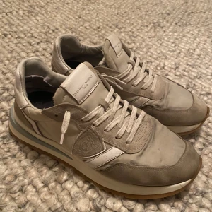 Beige Philippe Model sneakers - Snygga sneakers från Philippe Model i vitt och ljusgrått. Väldigt bra pris i och med att nypris ligger på ungefär 2799 kr. Skorna är använda och har minimala skavanker lite här och där, däremot inget som man märker av till vardags. I allmänhet ett par väldigt stabila och stilrena skor som passar till i princip allt. Storleken är 41 men passar även för 42. som bilderna visar finns det några slitningar av skon, därav det fantastiska priset. Skriv om du har vidare funderingar!