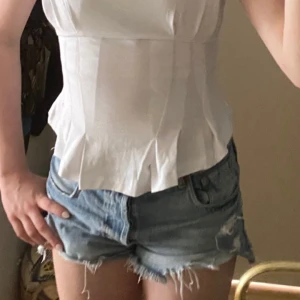 Vit korsett-topp med dragkedja Zara S - Superfräsch vit korsett-topp från Zara med markerad midja, veckade detaljer nertill och synlig dragkedja i ryggen. Ärmlös och figurnära passform som ger en clean och modern look. Perfekt att styla med jeans eller kjol för en trendig vibe. Helt oanvänd och med prislappen kvar! 