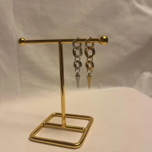 Chunky örhängen med kedjor och spikes - Säljer ett par coola örhängen med kedjelänkar i silver och guldton, avslutade med spetsiga spikes. Örhängena har ringar med små glittriga stenar upptill och hängande länkar som ger en edgy vibe. Perfekt för dig som gillar statement-smycken.