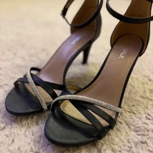Svarta klackar med glitter - Snygga svarta klackar från Walk i storlek 39 med smala remmar och glittrande strassdetalj över tårna. Skorna har öppen tå, smal klack och justerbart spänne runt ankeln.✨✨