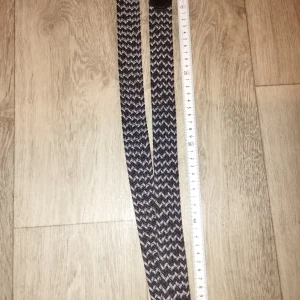 Svart och grått flätad bälte - Snyggt flätat bälte i svart och grått med ett coolt zigzag-mönster. Spännet är i mörk metall och bältet har detaljer i svart syntetmaterial. Perfekt för att ge outfiten lite edge och passar till både jeans och chinos.