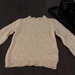 Beige stickad tröja med rund hals - Säljer en beige stickad tröja med rund hals och långa ärmar. Tröjan har ribbade muddar vid hals, ärmslut och nederkant. Perfekt för dig som gillar en enkel och klassisk look med mjuk känsla. Passar dig som vill ha en neutral färg i garderoben. Liten i storleken skulle säga en s