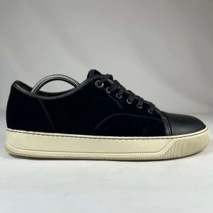  Lanvin - Snygga svarta sneakers från Lanvin med ovandel i mjuk mocka och tåparti i svart skinn. Skorna har snörning och en kontrasterande vit platt sula som ger en clean look. Perfekta för dig som gillar stilrena och exklusiva detaljer.