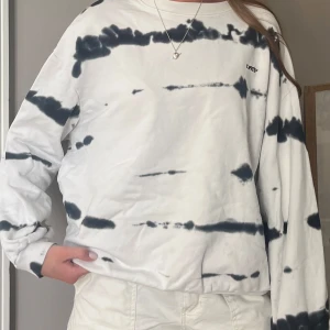 Vit och svart tie-dye sweatshirt - Säljer en oversized vit sweatshirt med svart tie-dye mönster från Levis. Tröjan har rund halsringning och långa ärmar. Perfekt för en avslappnad och trendig look.