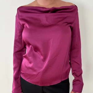 Mörklila offshoulder polotopp - Snygg mörklila topp med offshoulder-design och långärmade ärmar. Toppen har en slät, glansig yta.