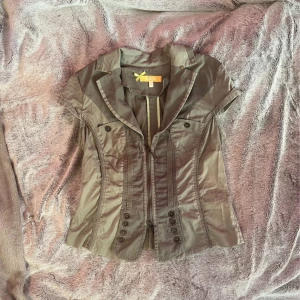 Grön kortärmad topp från BIBA - Snygg grön topp från BIBA med korta ärmar, markerad midja och coola detaljer som knappar framtill och fickor med lock. Toppen  är tillverkad i mjuk bomull med lite stretch för skön passform.