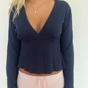 Mörkblå omlottopp med knyt - Snygg mörkblå omlottopp med v-ringning och långa ärmar. Toppen har ett croppat snitt och knyt i ryggen. Tillverkad i ett mjukt, lätt strukturerat bomullstyg som känns skönt mot huden. Modellen på bild är 171cm
