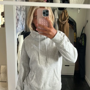 Grå hoodie från Ralph Lauren - Säljer en ljusgrå hoodie från Ralph Lauren med klassisk logga på bröstet. Tröjan har ingen luva med snörning, magficka och ribbade muddar vid ärmslut och nederkant. Perfekt för chill dagar och enkel att matcha med jeans eller mjukis.