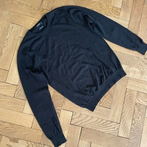 Stickad Tiger of Sweden tröja - Svart stickad tröja från Tiger of Sweden i storlek M, tillverkad av fin italiensk garn. Klassisk rund hals och ribbade muddar. Tröjan har lång ärm med snygga svarta armbågslappar som ger en cool detalj. Perfekt för dig som gillar stilrena och enkla plagg. Pris är inte hugget i sten. Vid minsta beundran hesitera inte att fråga.