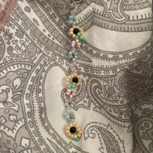 Färgglad keychain för mobilskal 🌻 - Superfint handgjort armband med små pärlor i pastellfärger och blommönster. Pärlorna är i ljusgul, mintgrön, ljusblå, rosa och svart, och armbandet har en söt och lekfull vibe. Perfekt för dig som gillar unika accessoarer med blommig design.